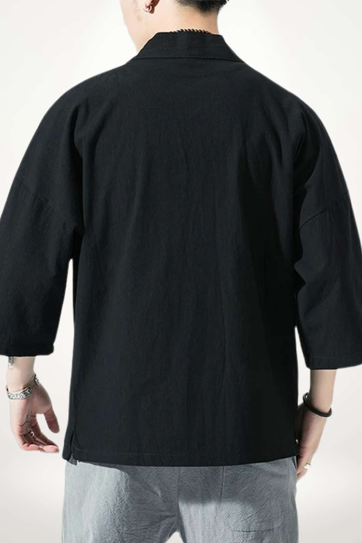Homme de dos portant un kimono noir à manches larges, avec un fond clair et un décor minimaliste