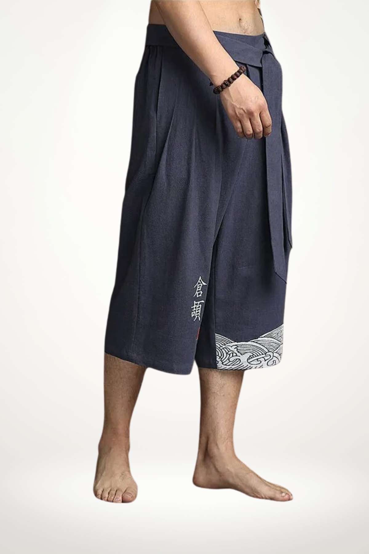 Pantalon kimono homme en tissu bleu foncé, avec un motif ondulé blanc sur le bas, porté pieds nus