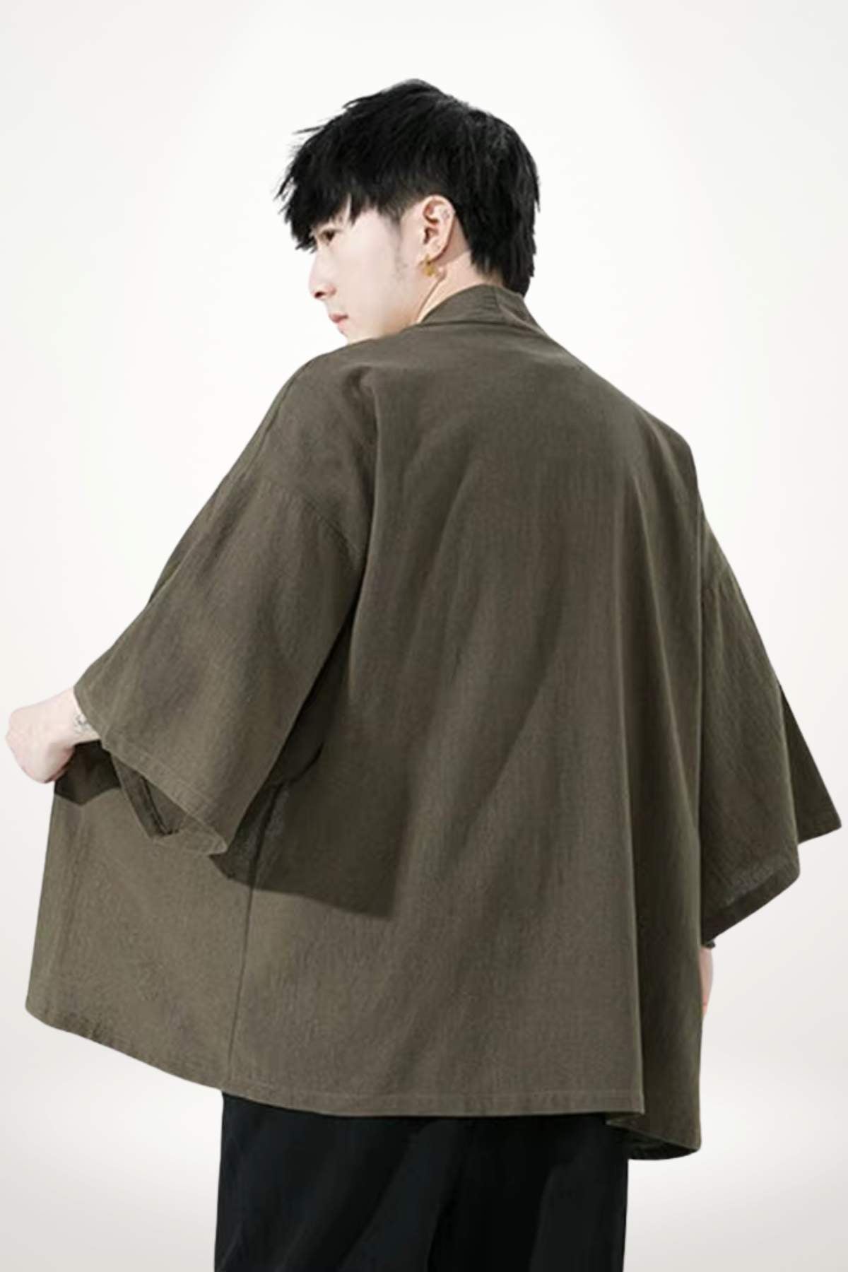 Homme portant un kimono moderne en tissu olive, avec des manches larges, se tenant de dos sur fond neutre