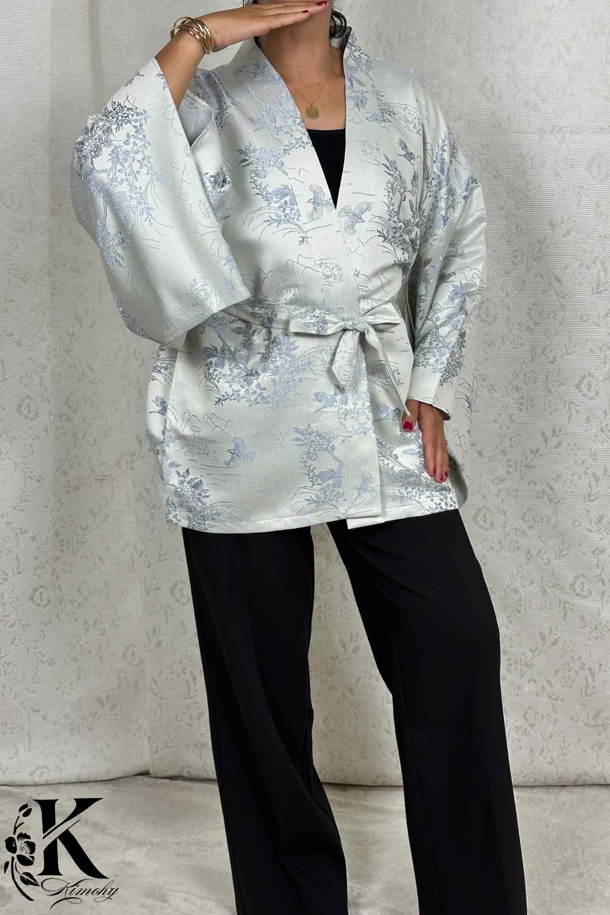 Femme portant un kimono gris clair avec motifs floraux bleus, associé à un pantalon noir, en pose élégante