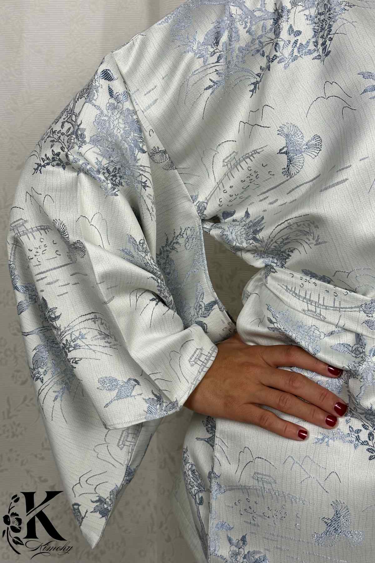 Kimono féminin en satin blanc avec motifs floraux et oiseaux bleus, porté avec une main sur la taille