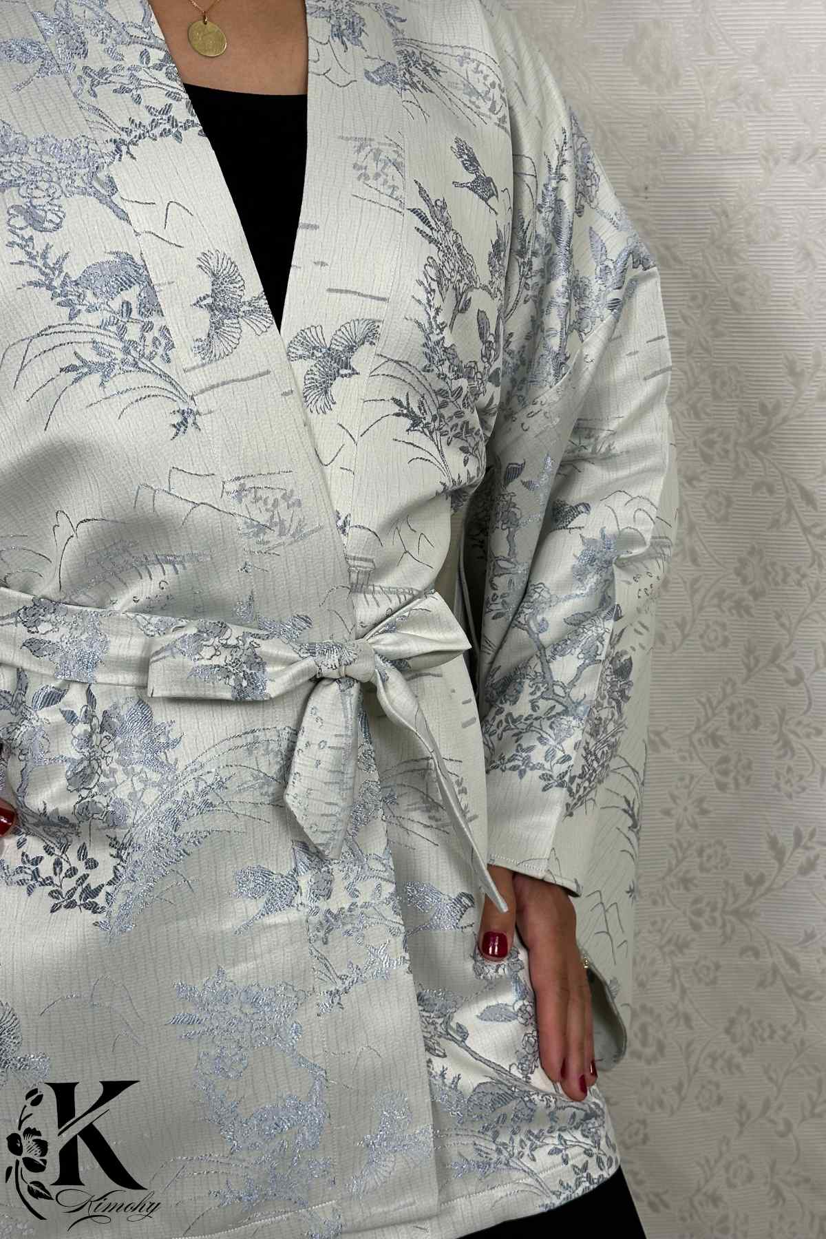 Kimono en satin clair avec motifs floraux et oiseaux, ceinturé à la taille, porté sur un fond texturé
