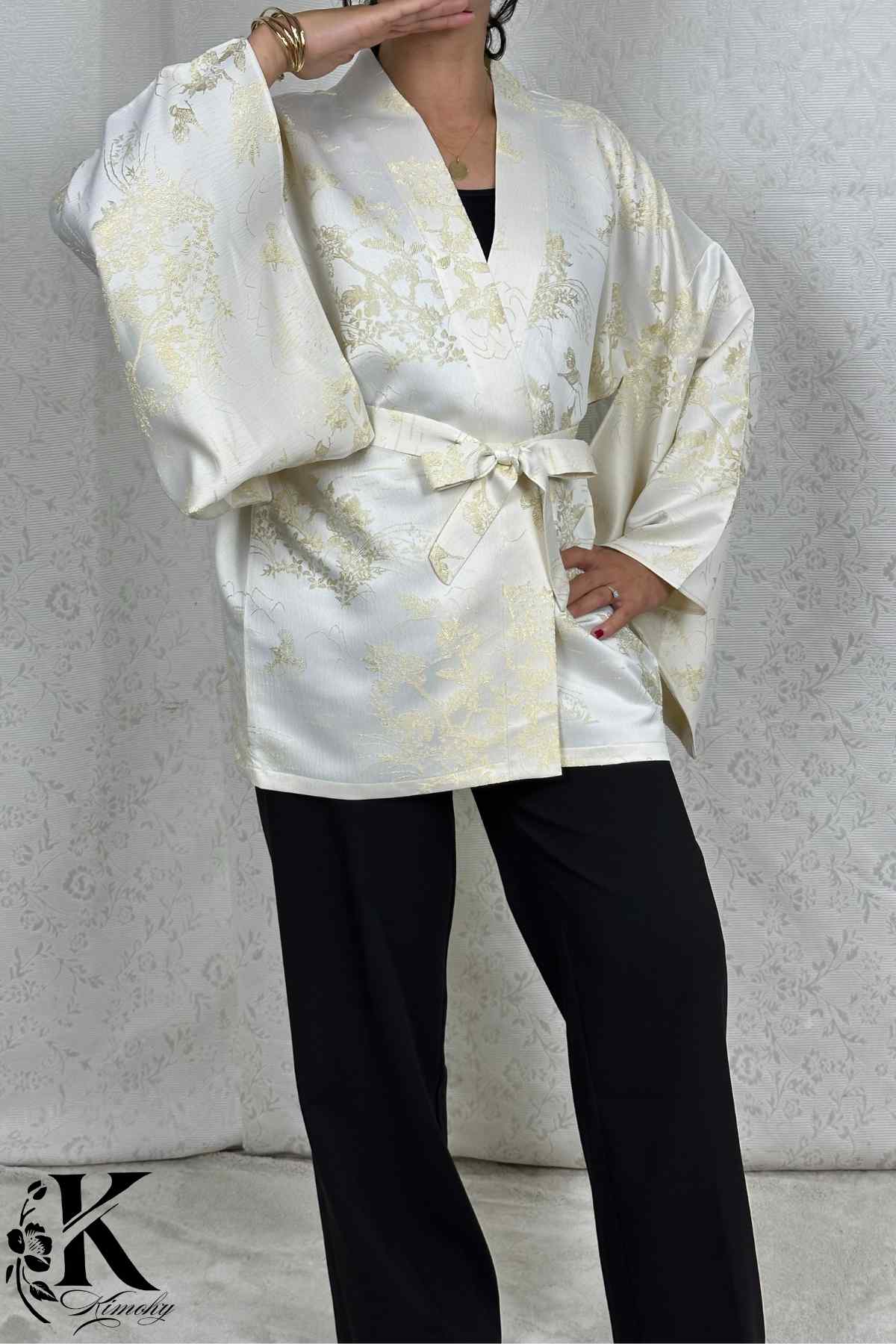 Femme portant un kimono blanc avec des motifs dorés, ceinturé, sur un fond décoratif clair et texturé