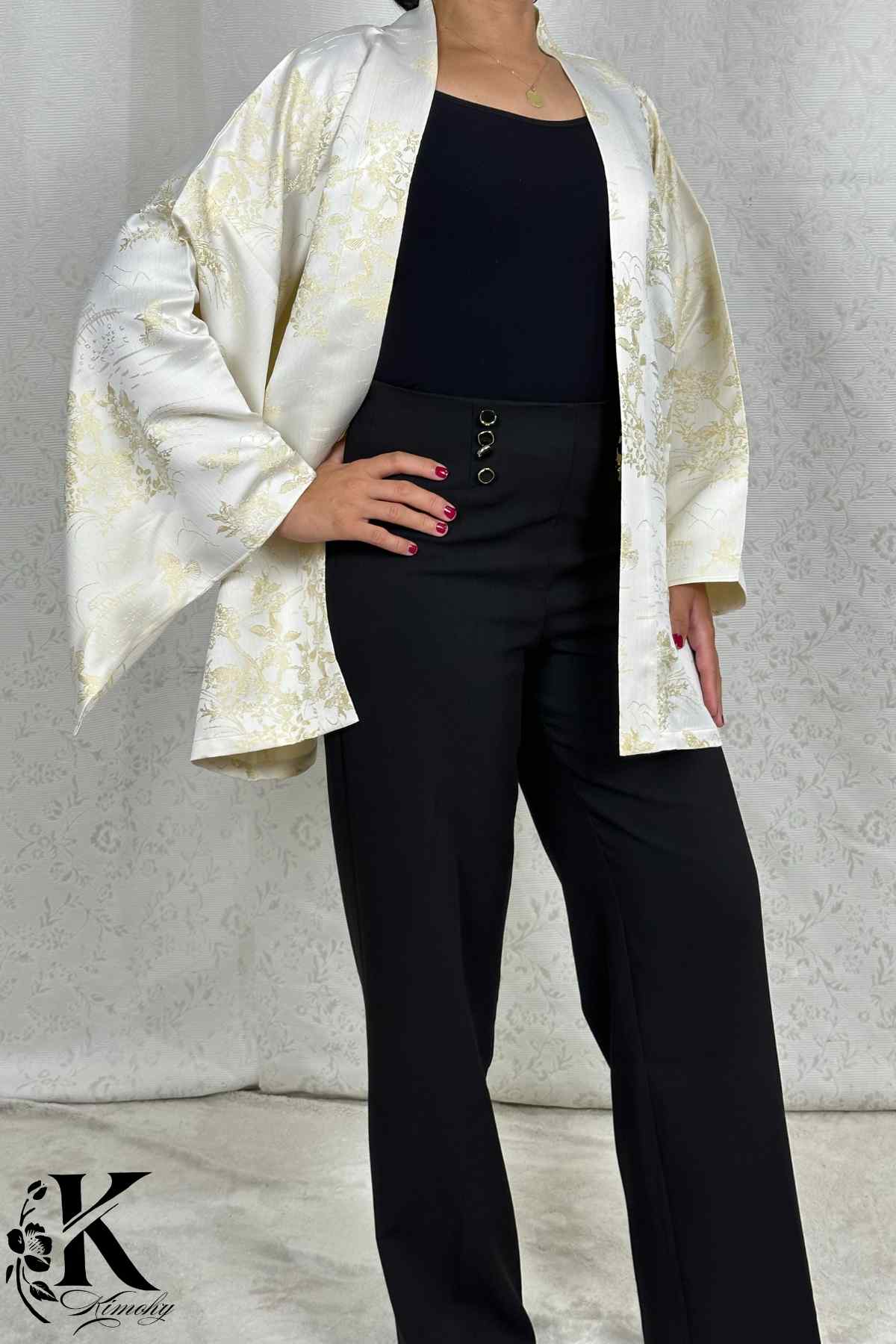 Femme portant un kimono blanc à motifs dorés, avec un pantalon noir, dans un décor sobre et élégant