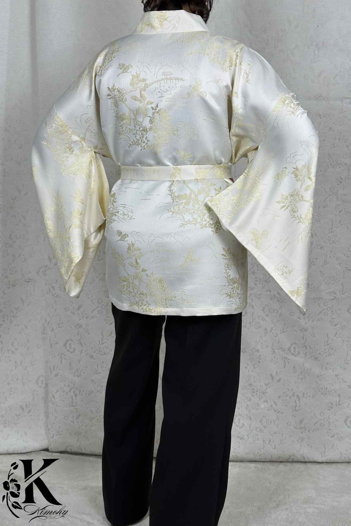 Kimono chic en satin blanc avec motifs dorés, porté avec un pantalon noir, dans un décor sobre et élégant