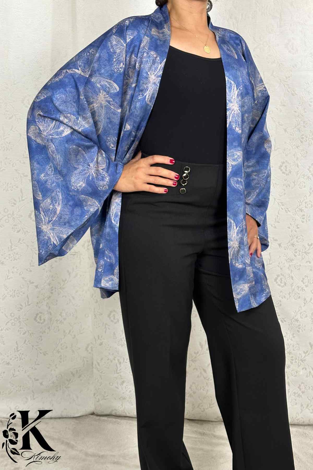 Femme portant un kimono bleu floral avec des motifs de papillons, associé à un pantalon noir élégant