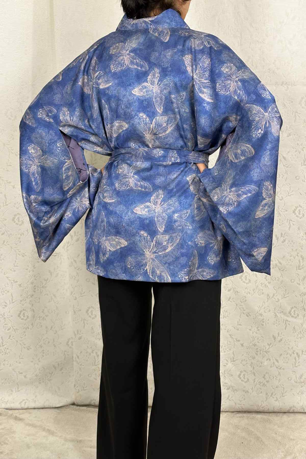 Kimono bleu avec motifs de papillons, manches larges, ceinture nouée, porté avec un pantalon noir, fond clair