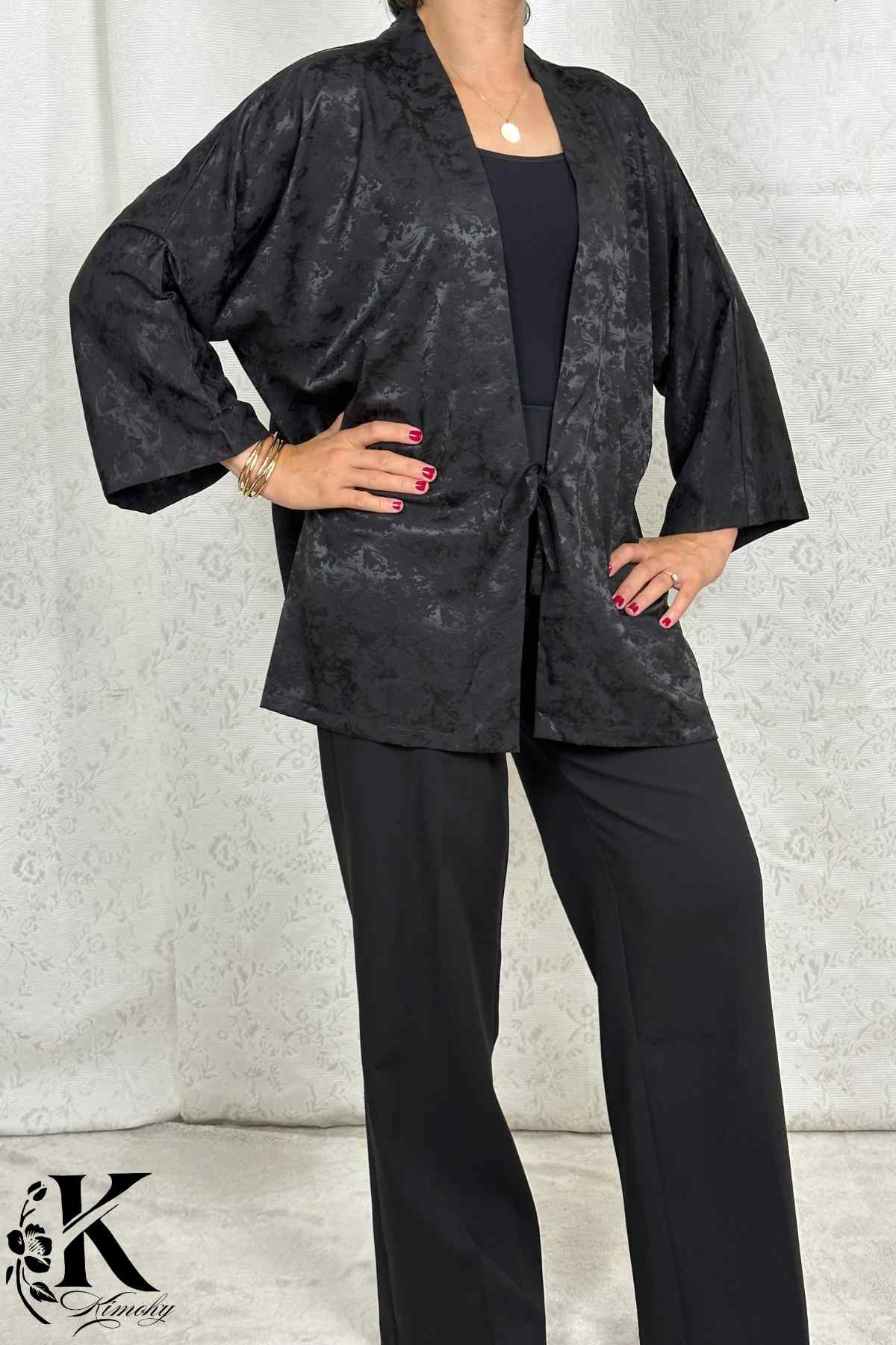 Femme en kimono noir avec motifs subtils, posant avec élégance sur fond clair et décor floral