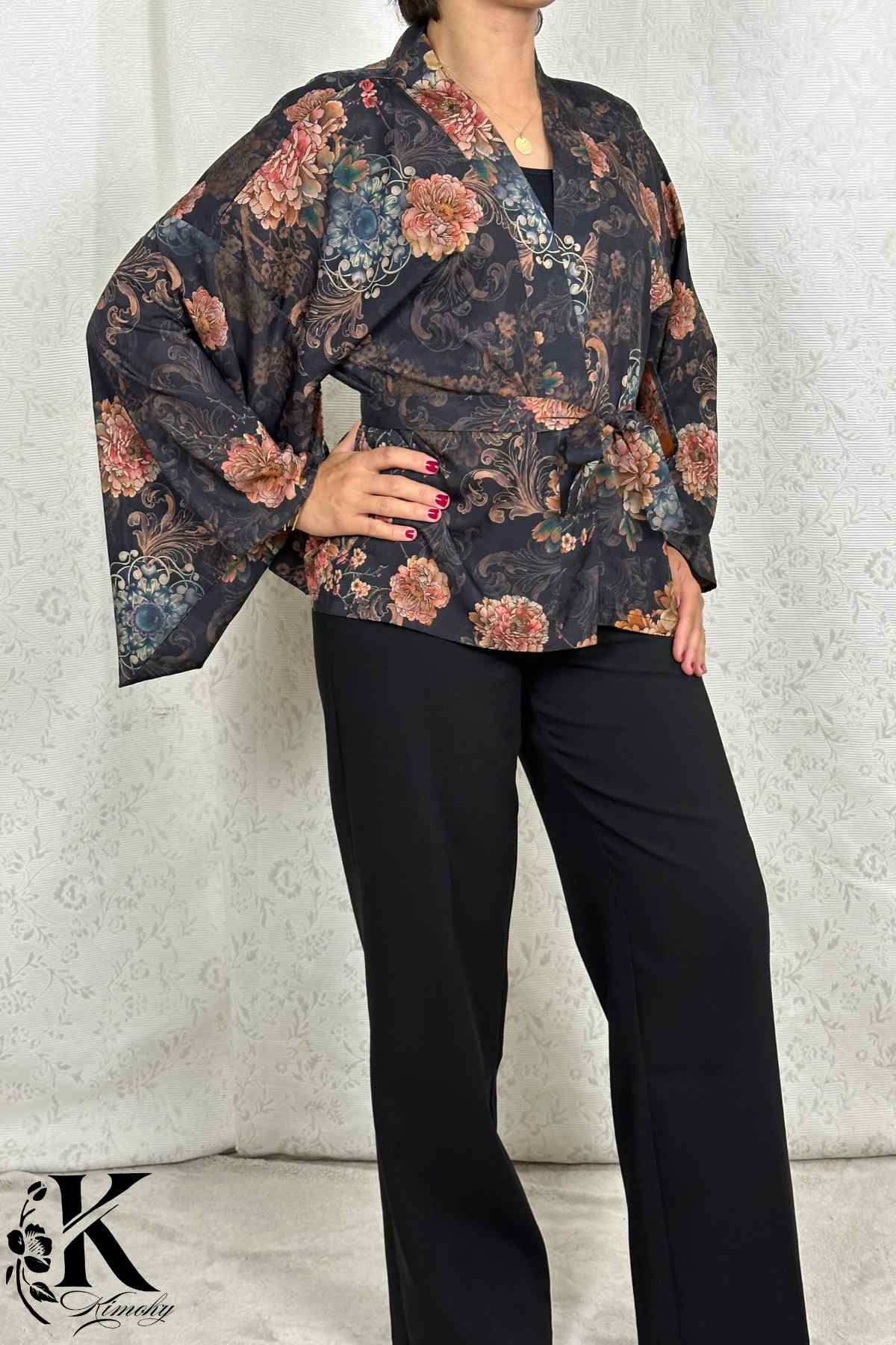 Femme portant un kimono noir à motifs floraux, avec des manches larges, dans un décor sobre et élégant