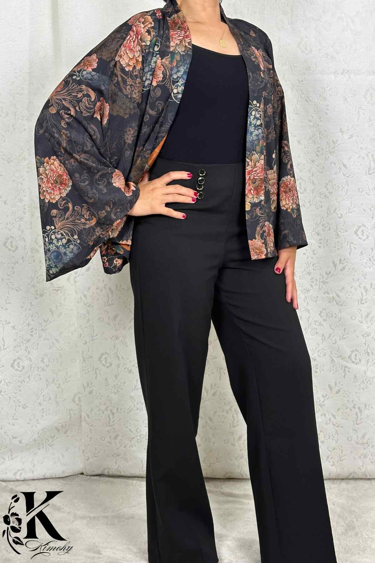 Femme portant un kimono à motifs floraux sur fond noir, avec un pantalon noir élégant, dans un décor sobre