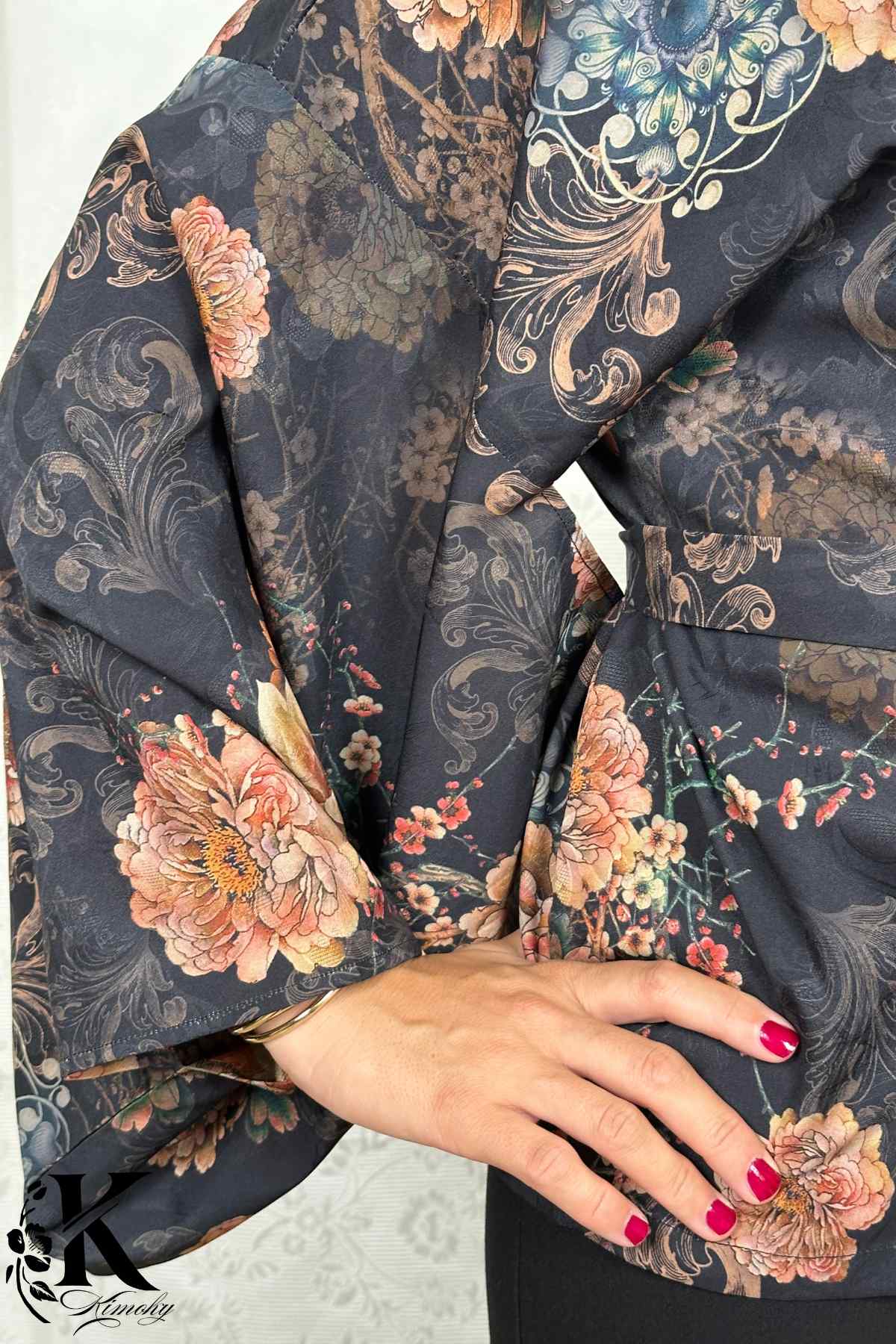 Kimono élégant à motifs floraux colorés sur fond noir, porté avec une main posée sur la taille