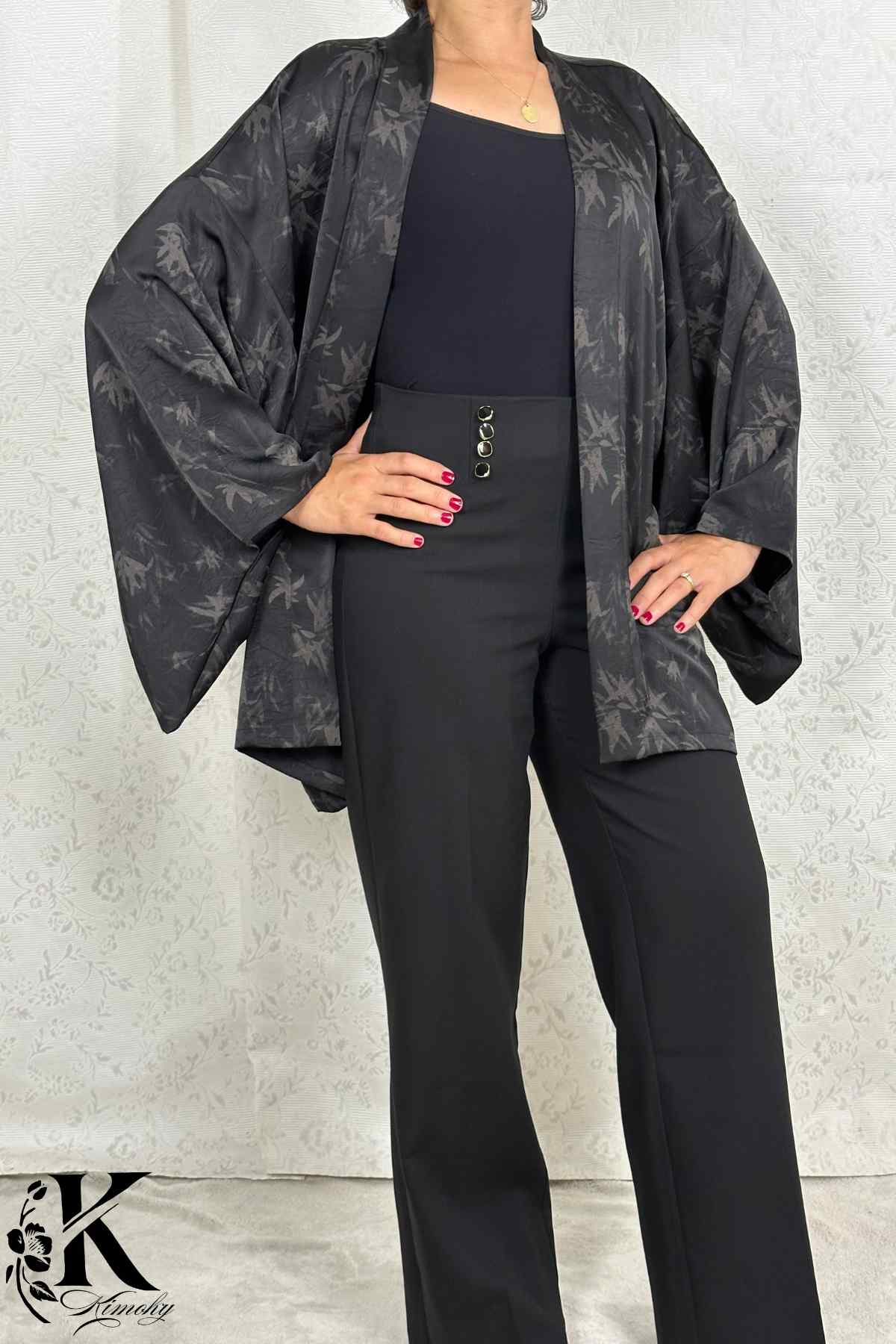 Femme portant un kimono noir à motifs, avec un pantalon noir, dans un décor sobre et élégant