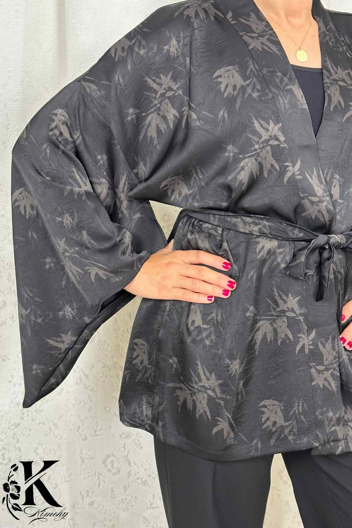 Kimono noir à motifs de feuilles, ceinturé à la taille, porté avec un fond clair et décor élégant