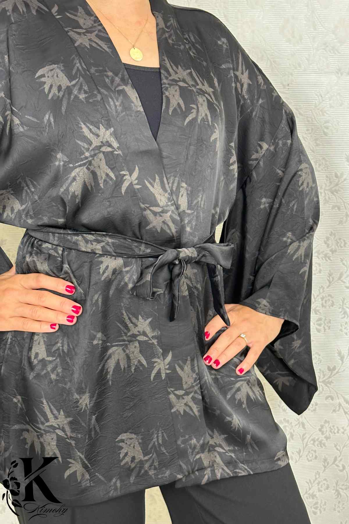 Kimono noir avec motifs de feuilles grises, ceinturé, porté par une femme dans un décor sobre