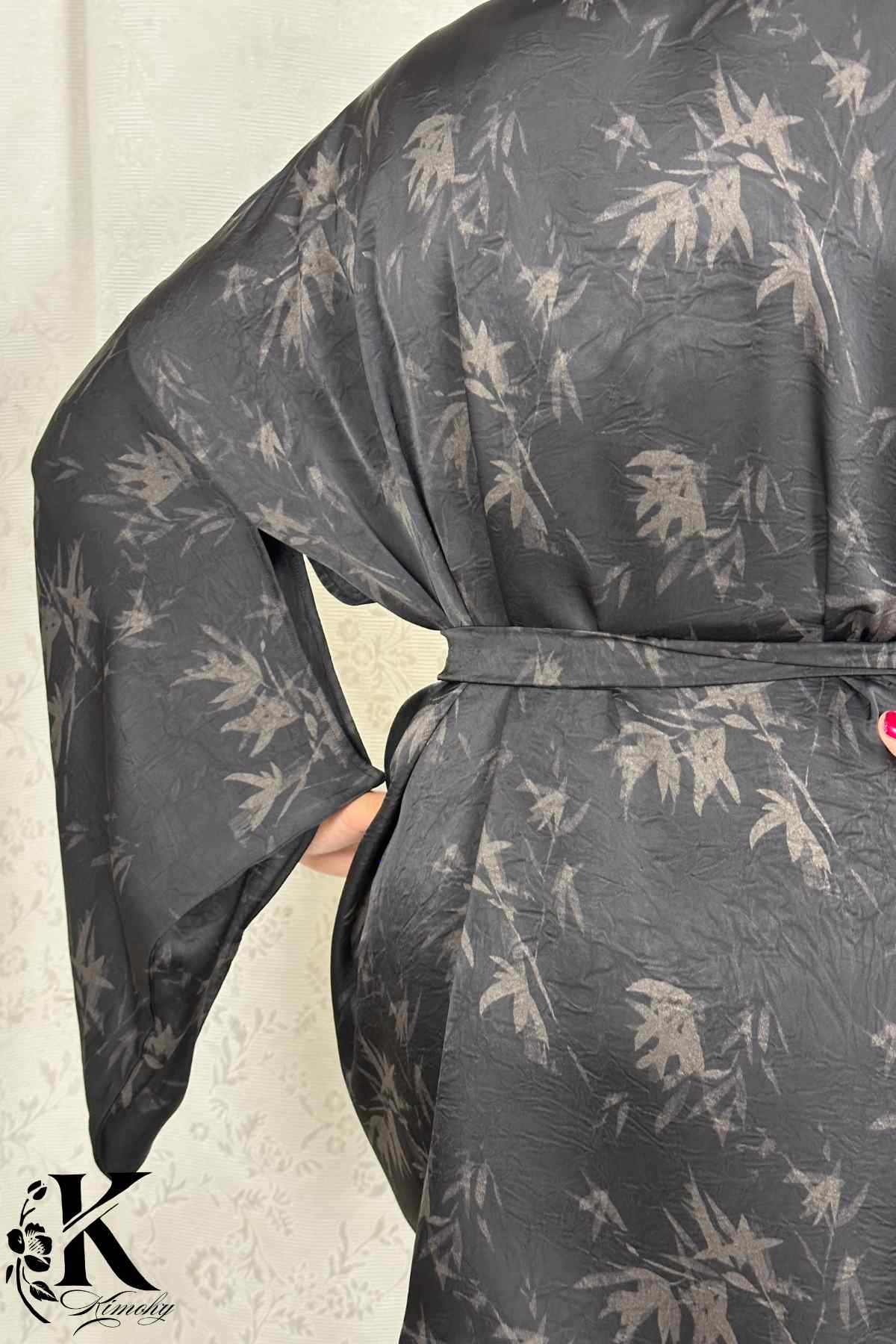 Kimono noir à motifs de feuilles grises, avec une ceinture, porté dans un décor sobre et élégant