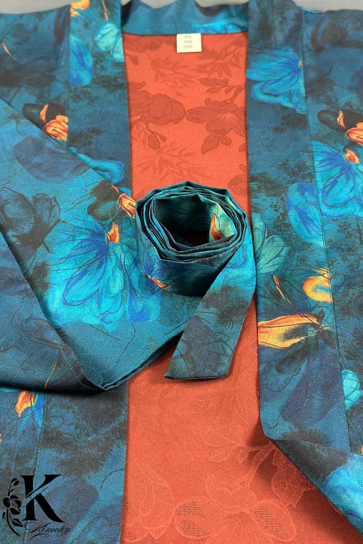 Kimono en satin bleu avec motifs floraux, doublure orange, posé sur un fond texturé