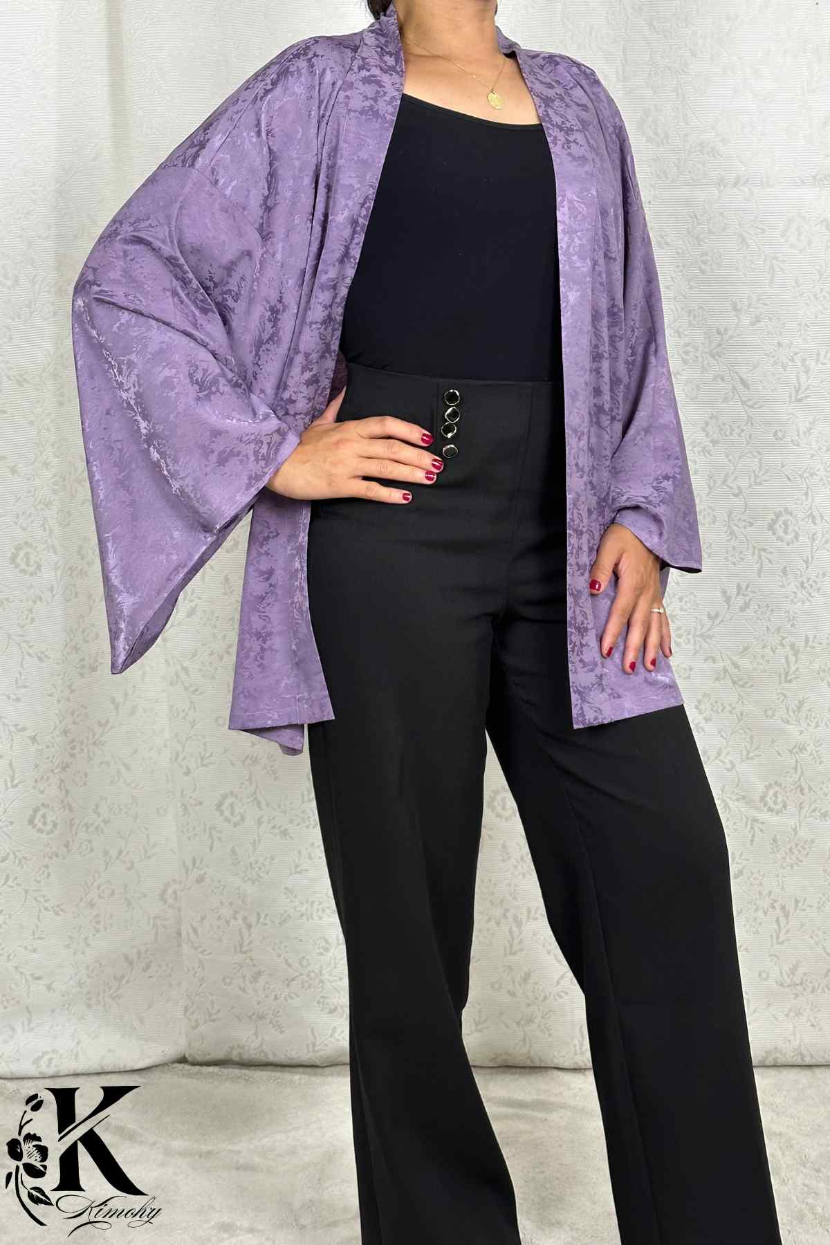 Veste kimono femme en satin violet, manches larges, portée avec un pantalon noir, fond décoratif clair