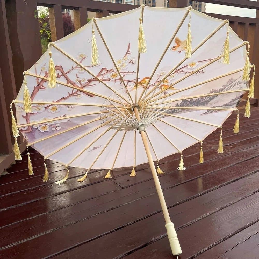 Ombrelle japonaise ornée de fleurs et de motifs délicats, avec des franges dorées, posée sur un sol en bois