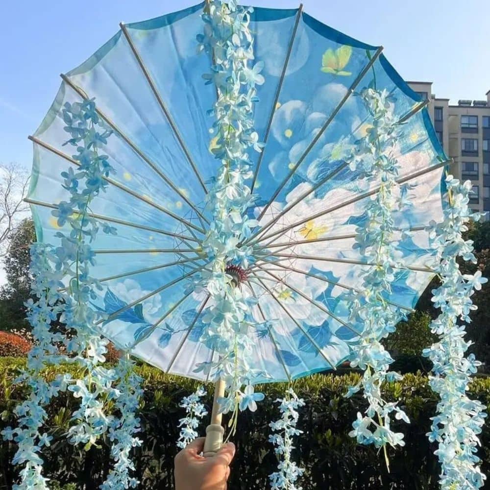 Ombrelle anti-UV bleue ornée de fleurs, avec un motif nuageux et une structure en bois, tenue à la main