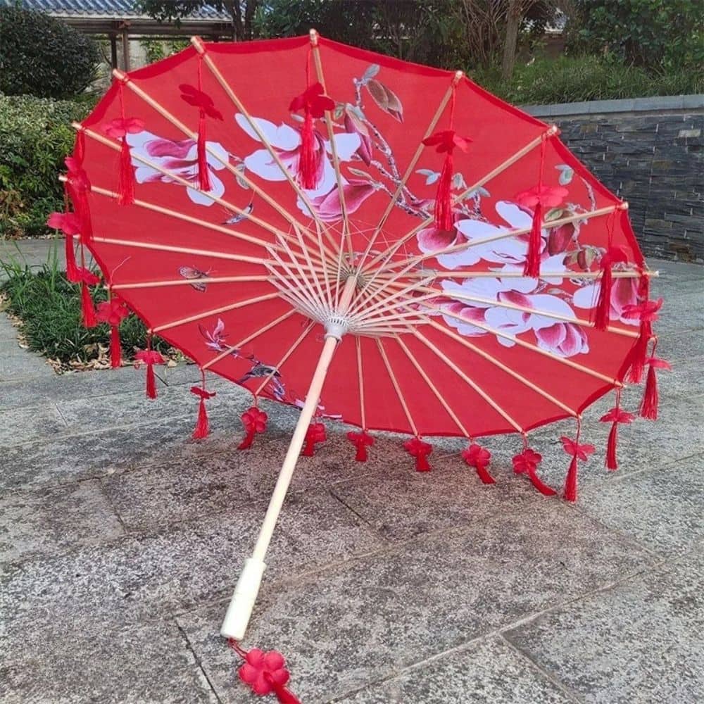 Ombrelle universelle anti UV rouge ornée de motifs floraux, posée sur un sol en pierre grise