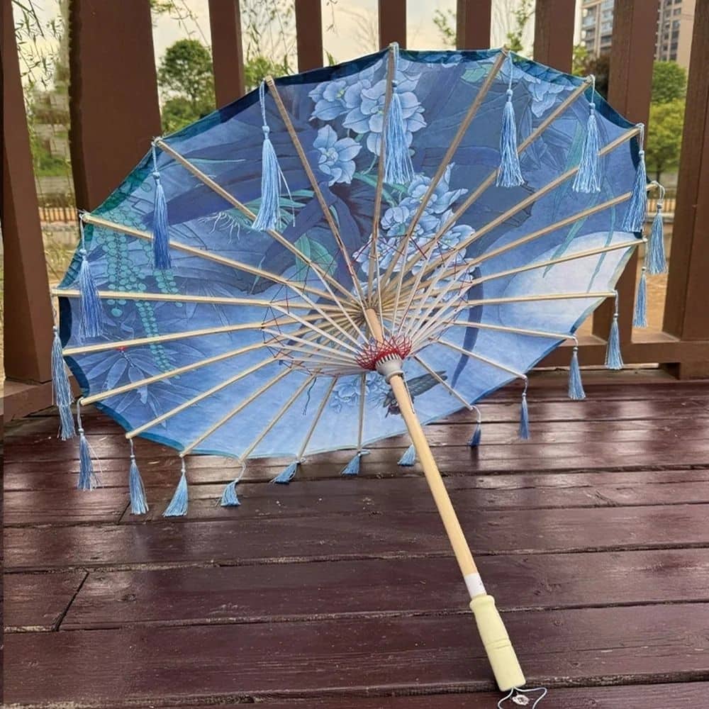 Ombrelle d'été en bleu avec motifs floraux, décorée de franges, posée sur un sol en bois