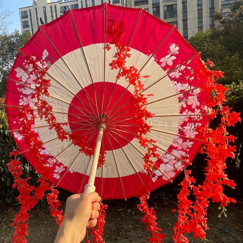 Ombrelle rouge et blanche ornée de fleurs, tenue à la main, avec un décor urbain en arrière-plan