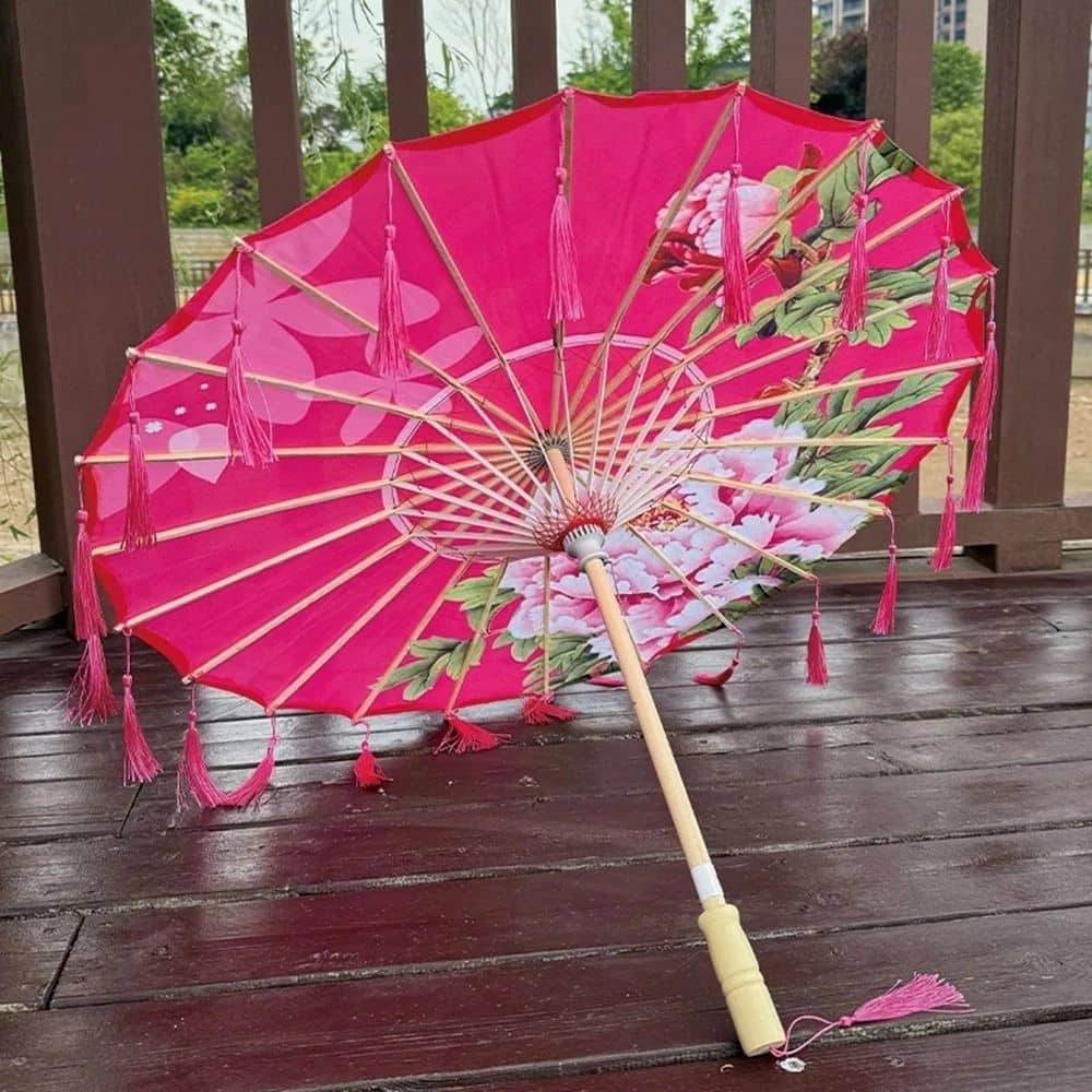 Ombrelle japonaise en papier rose ornée de motifs floraux, posée sur un sol en bois