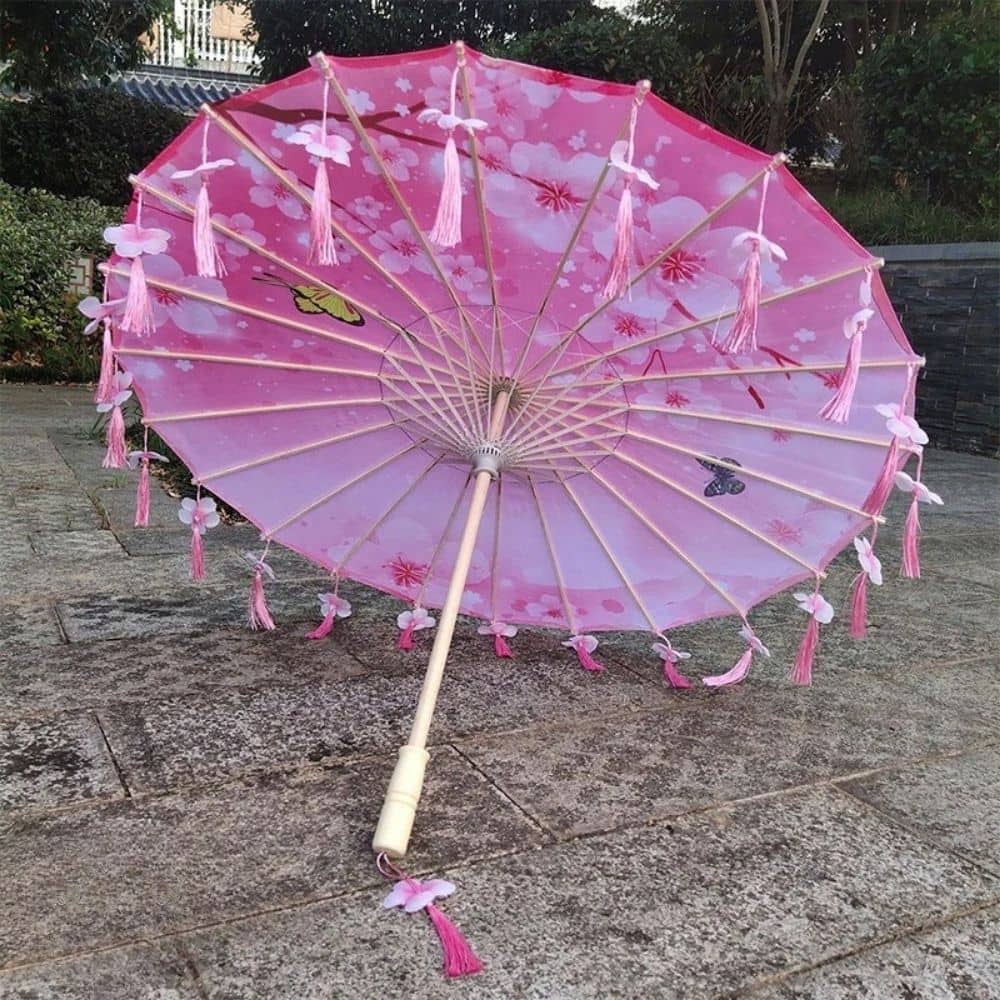 Parapluie japonais rose décoré de pompons et de motifs floraux, reposant sur un sol en pierre