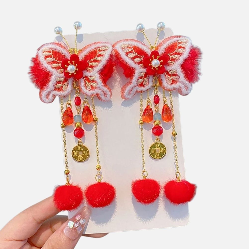 Bijoux en forme de papillon rouge avec perles et pompons, sur fond blanc, tenant dans une main