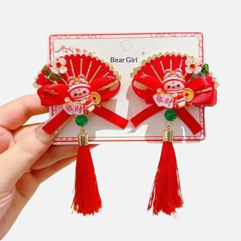 Deux broches décoratives rouges avec des motifs dorés, un personnage en céramique et des pompons en franges