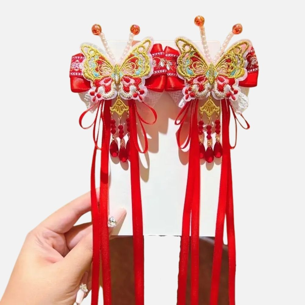 Deux ornements en forme de papillon, rouges et dorés, avec des rubans et des perles suspendus