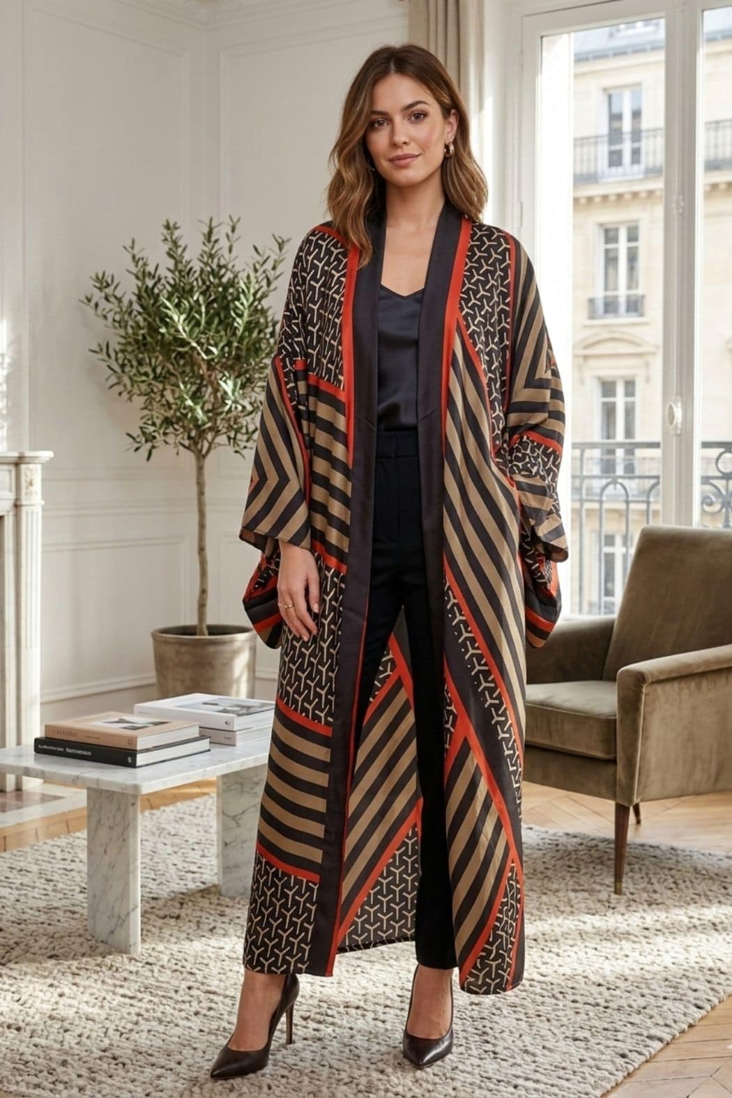 Femme portant un cardigan kimono aux motifs géométriques noirs, marron et rouges, dans un intérieur lumineux et élégant
