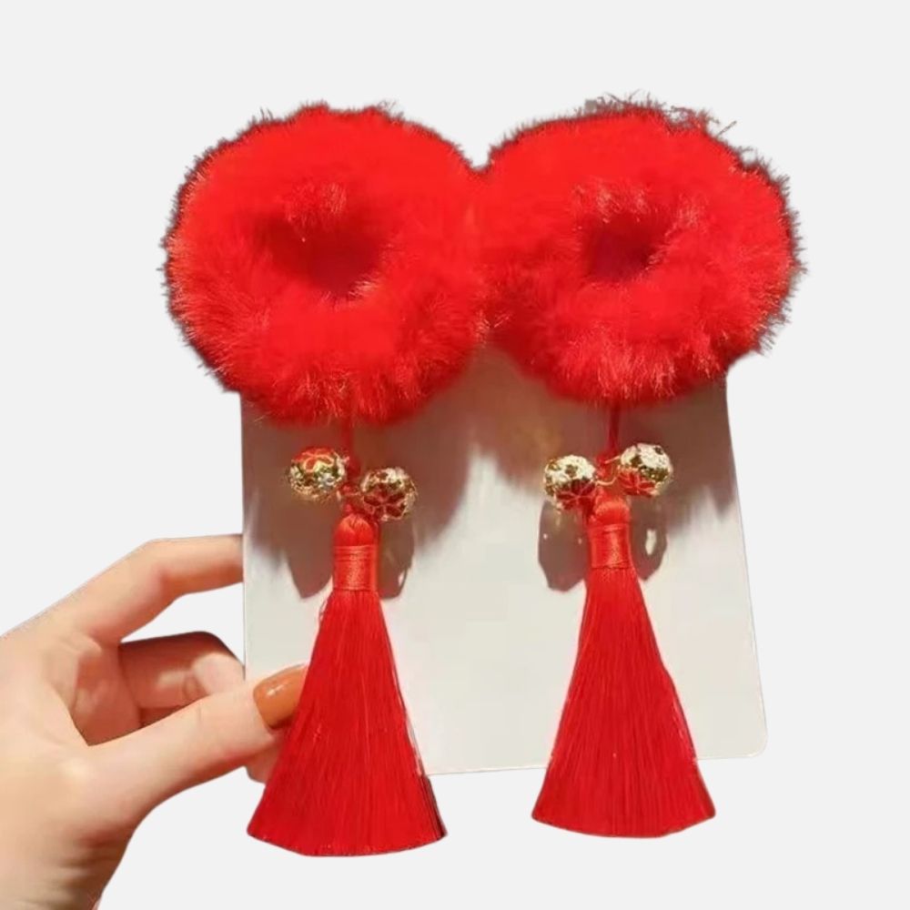Deux accessoires en rouge vif avec des pompons en fourrure et des franges, ornés de perles dorées