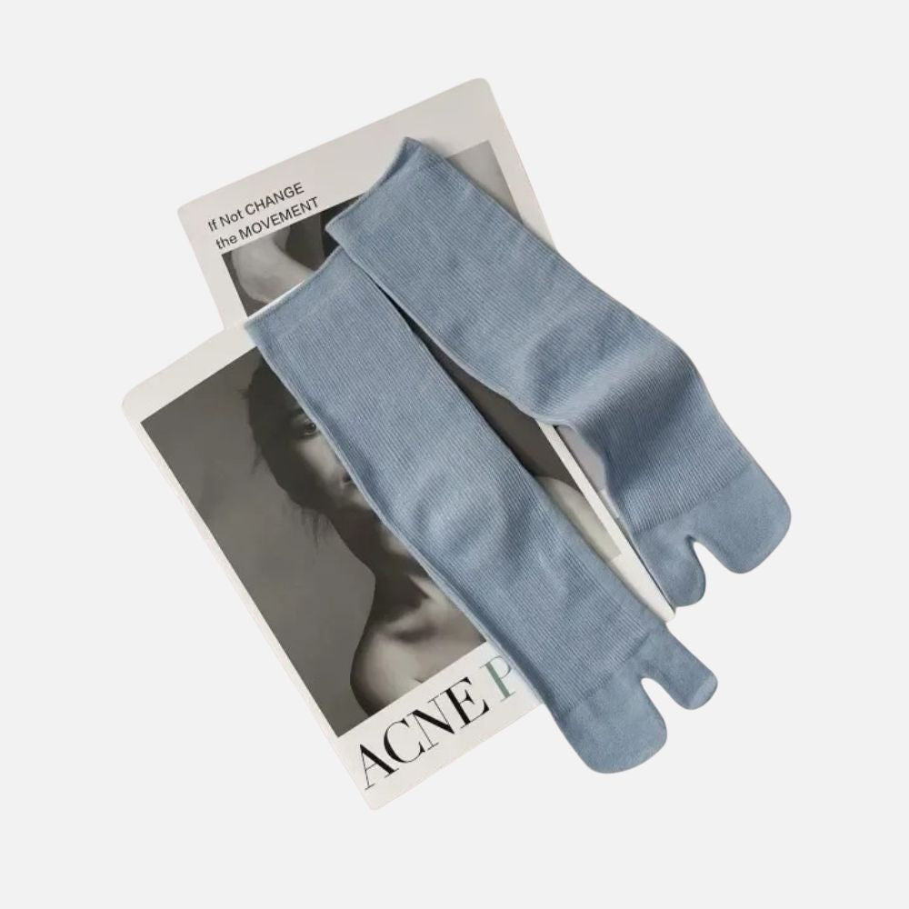 Chaussettes tabi bleu ciel en matière douce posées sur un magazine en noir et blanc, créant un contraste élégant