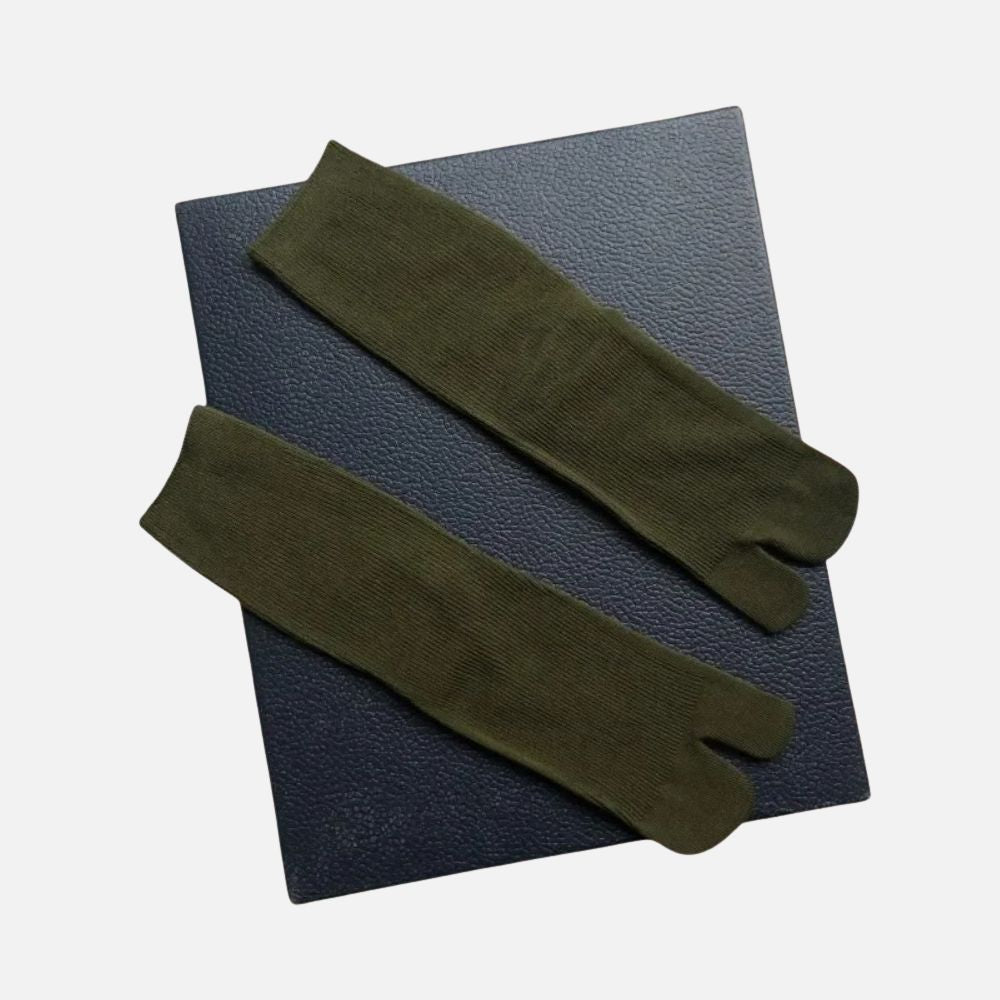 Chaussettes tabi kaki en matière douce, posées sur un fond noir texturé, avec une coupe traditionnelle