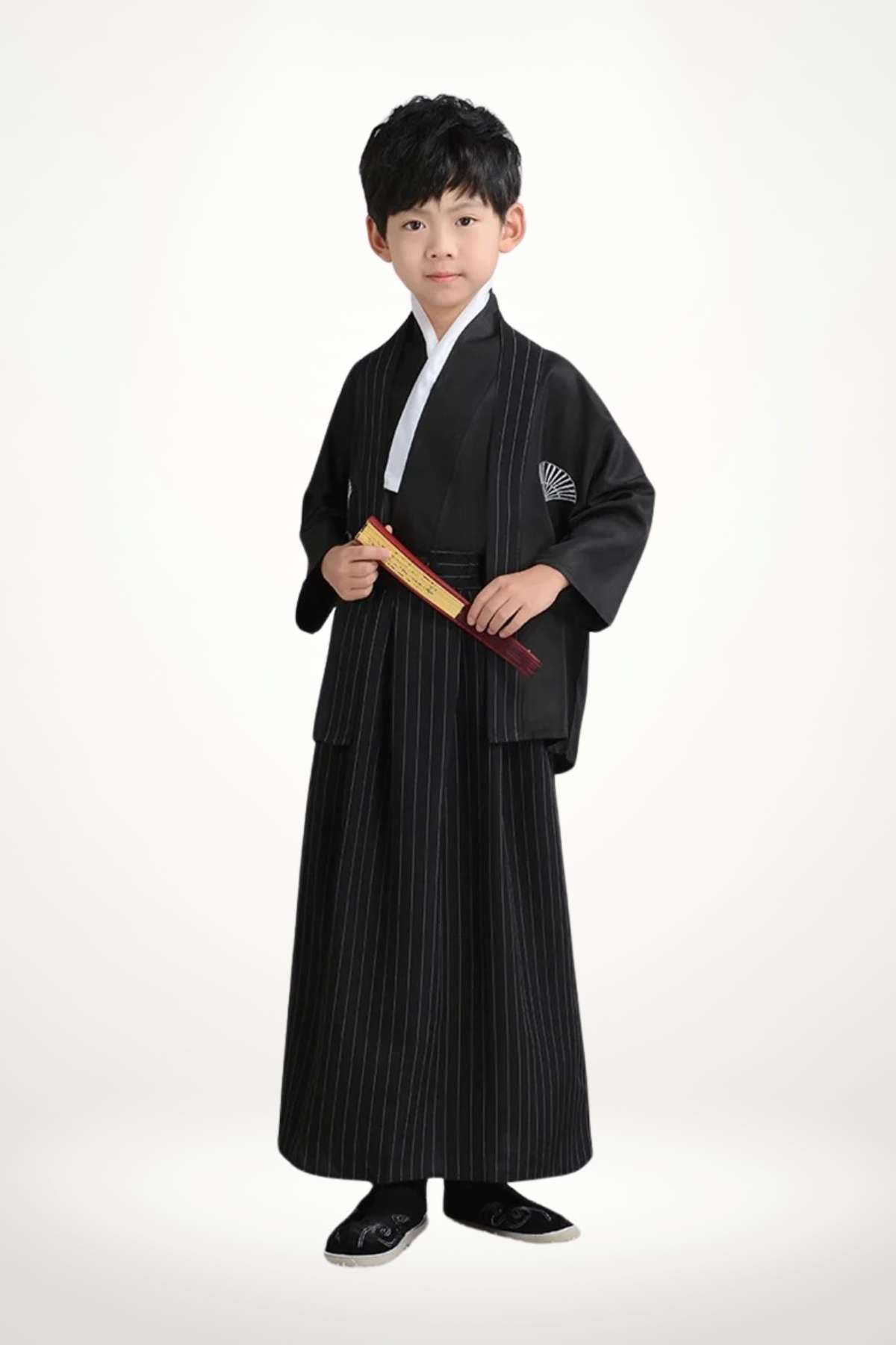 Un enfant porte un kimono noir à rayures avec un col blanc et des chaussons noirs, se tenant droit