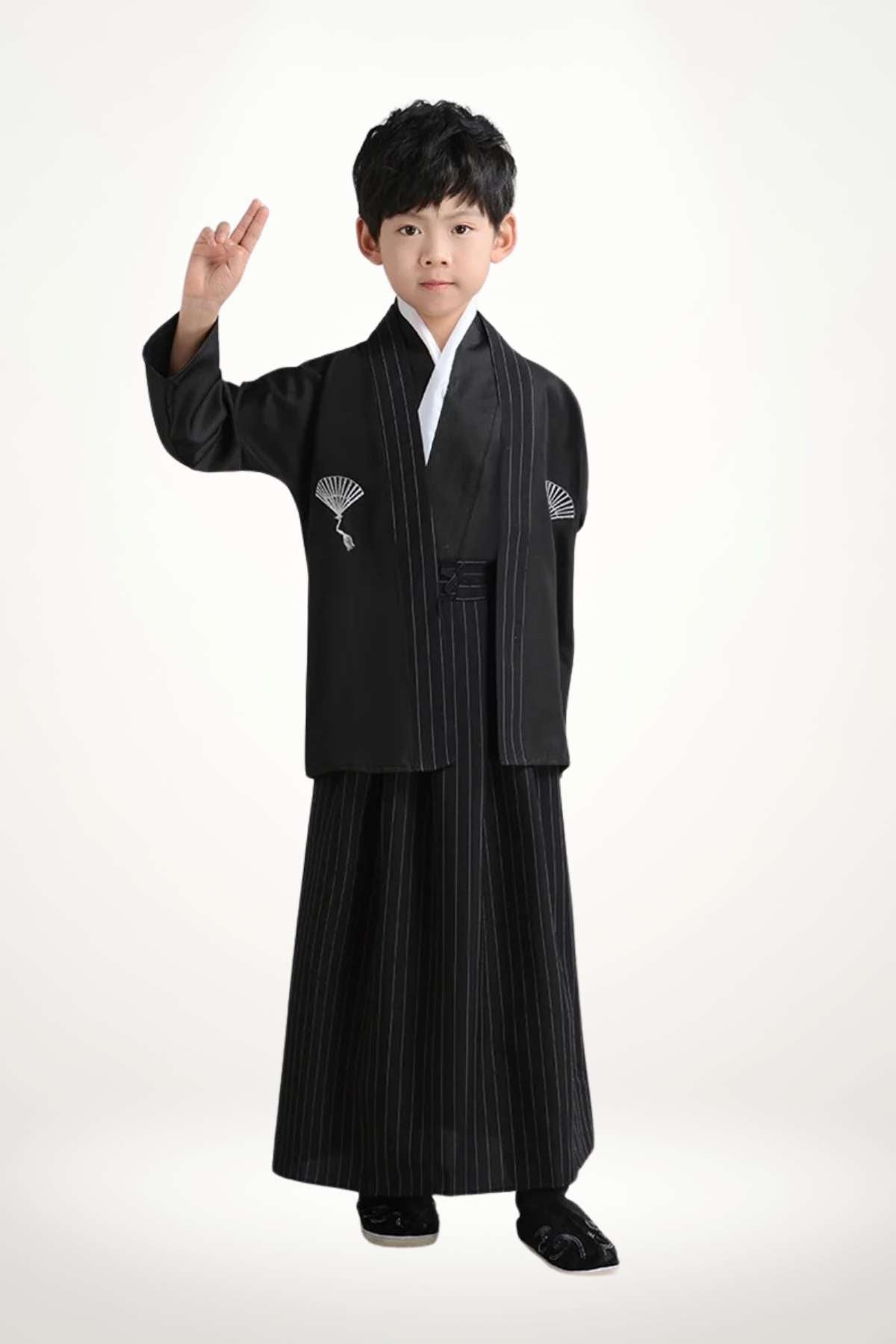 Enfant portant un kimono noir avec des motifs en éventail, debout avec un geste de paix sur fond clair