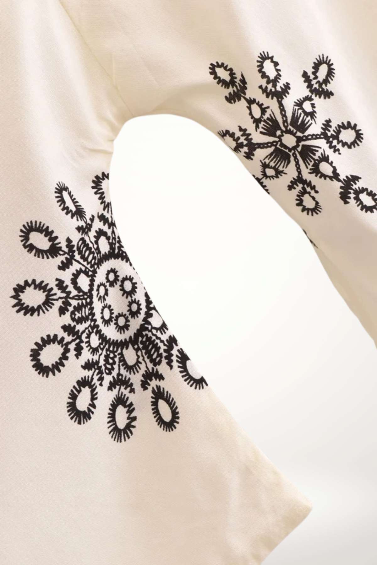 Un kimono léger en tissu crème avec des motifs floraux noirs sur les manches, évoquant un style bohème