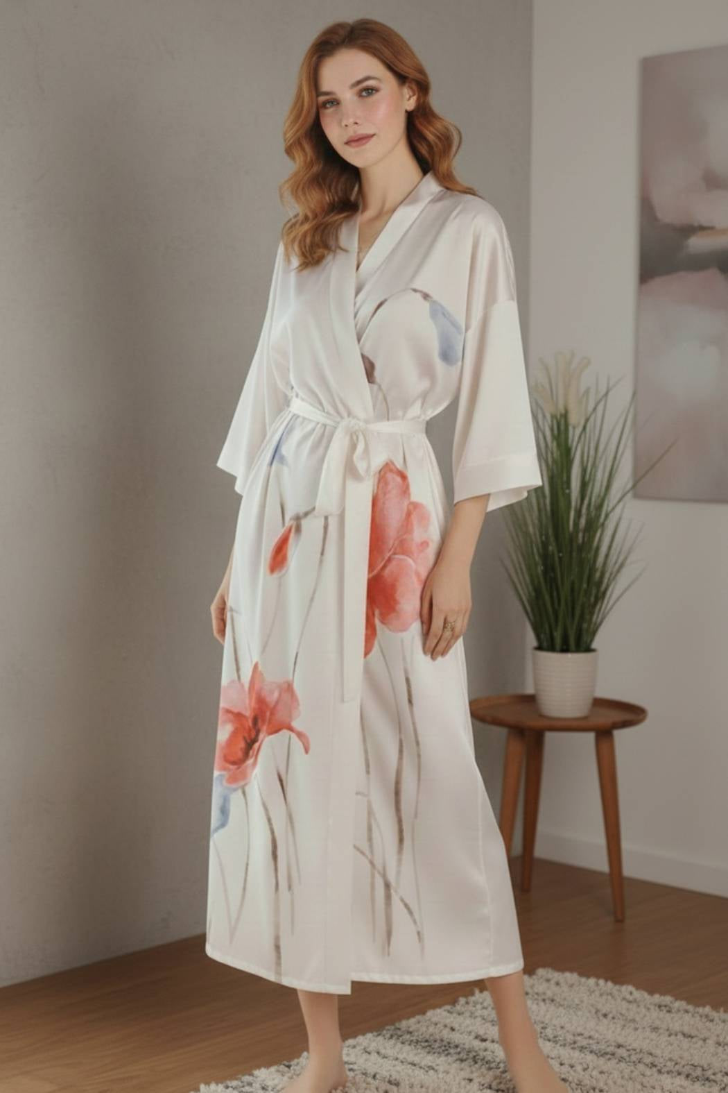 Femme en kimono blanc satiné avec motifs floraux rouges et bleus, posant dans un décor moderne et épuré