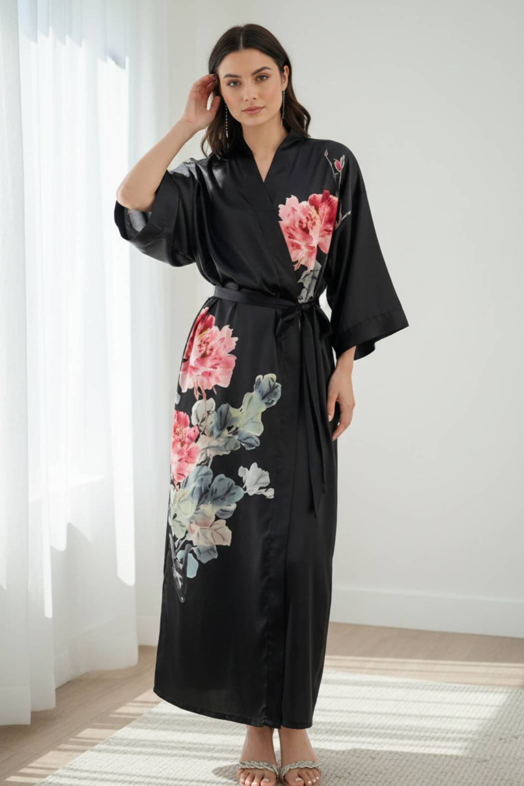 Femme en kimono noir en satin avec motifs floraux roses, posant dans un intérieur lumineux et moderne