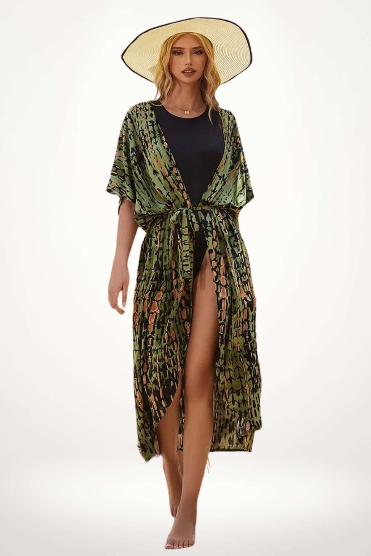 Femme en kimono vert à motifs, debout sur une plage, portant un chapeau large, avec une allure élégante