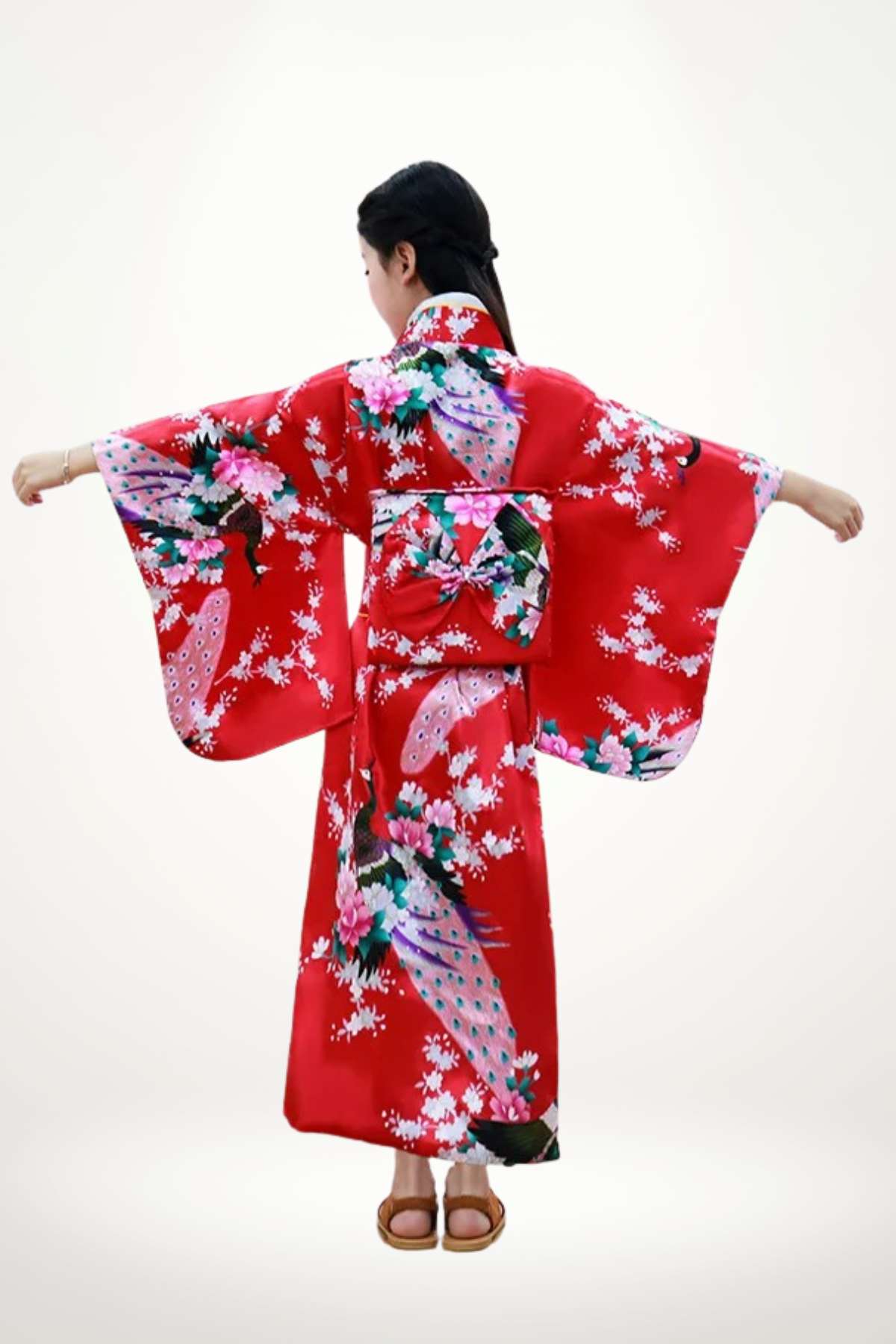 Fille portant un kimono rouge vif orné de fleurs roses et de motifs colorés, bras écartés dans un décor neutre