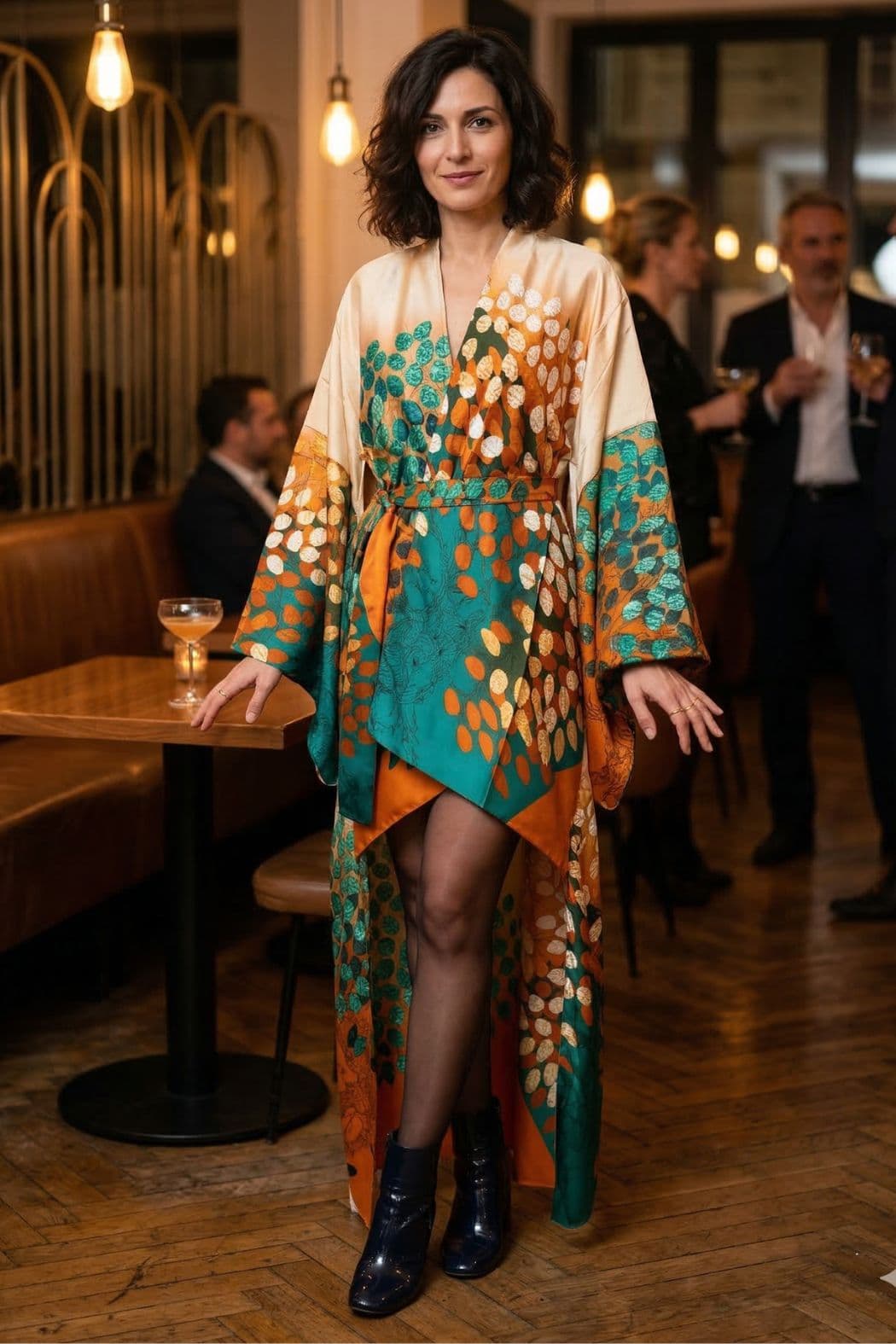 Femme en kimono satin aux motifs colorés, posant dans un décor chaleureux avec des lumières tamisées et des tables en