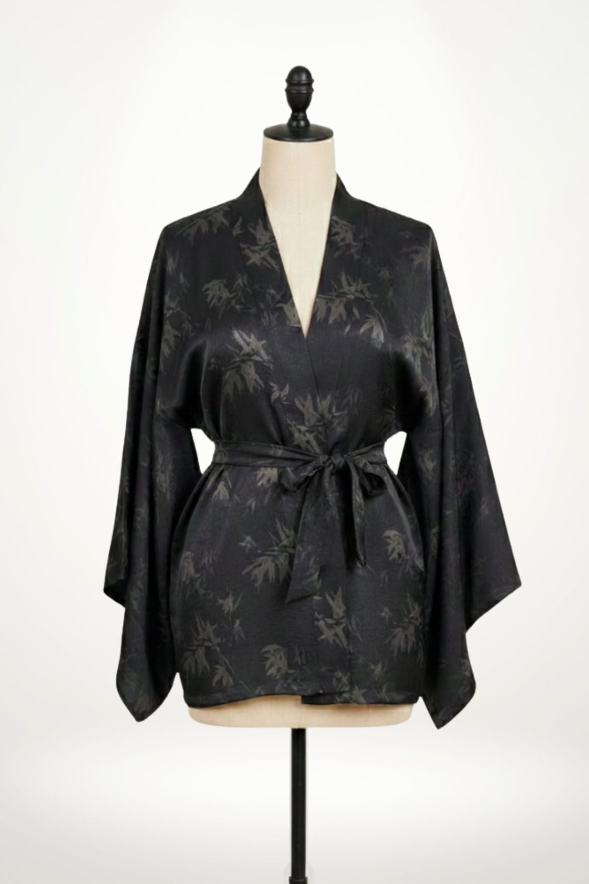 Femme en kimono noir à motifs de feuilles, posant dans un décor clair avec des motifs subtils