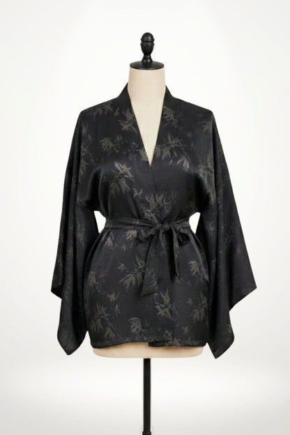 Femme en kimono noir à motifs de feuilles, posant dans un décor clair avec des motifs subtils