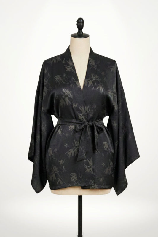 Femme en kimono noir à motifs de feuilles, posant dans un décor clair avec des motifs subtils