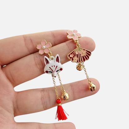 Boucles d'oreilles en métal doré avec un motif de renard blanc et des fleurs roses, évoquant un style japonais.