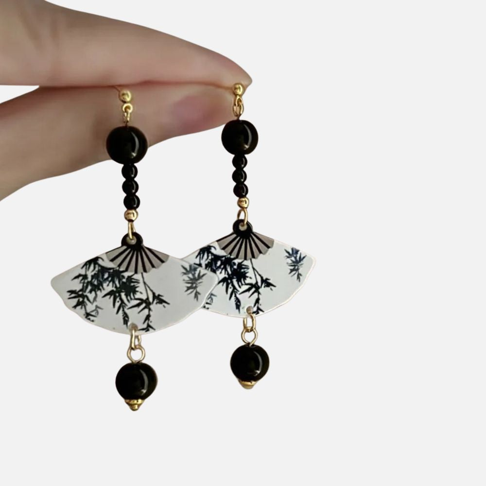 Boucles d'oreilles en forme d'éventail, avec motifs de bambou sur fond blanc et perles noires, évoquant le style japonais.