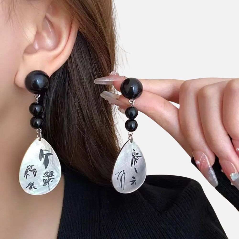 Boucles d'oreilles en nacre avec motifs floraux, perles noires brillantes, portées par une femme en pull noir, style japonais.