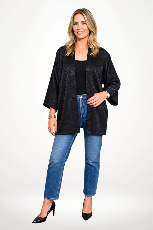 Femme en kimono noir avec motifs subtils, posant dans un décor clair et élégant, portant un pantalon noir